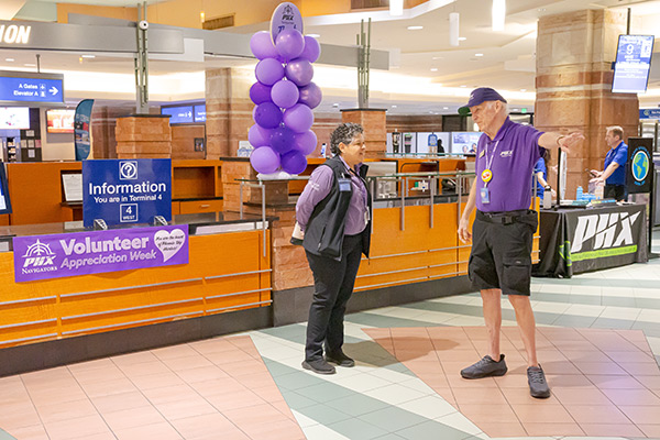 Two Navigator volunteers standing and talking to each other in front of an information desk in Terminal 4