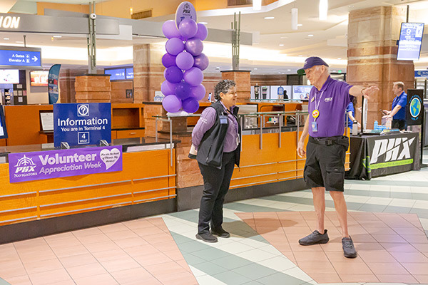 Two Navigator volunteers standing and talking to each other in front of an information desk in Terminal 4 Phoenix Sky Harbor Volunteers Celebrated During Appreciation Week