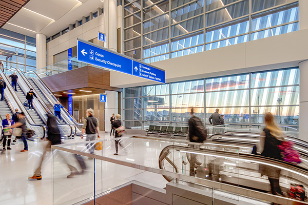 A scene inside Terminal 3 with travelers going up and down the escalators and a beautiful sunset outside the windows