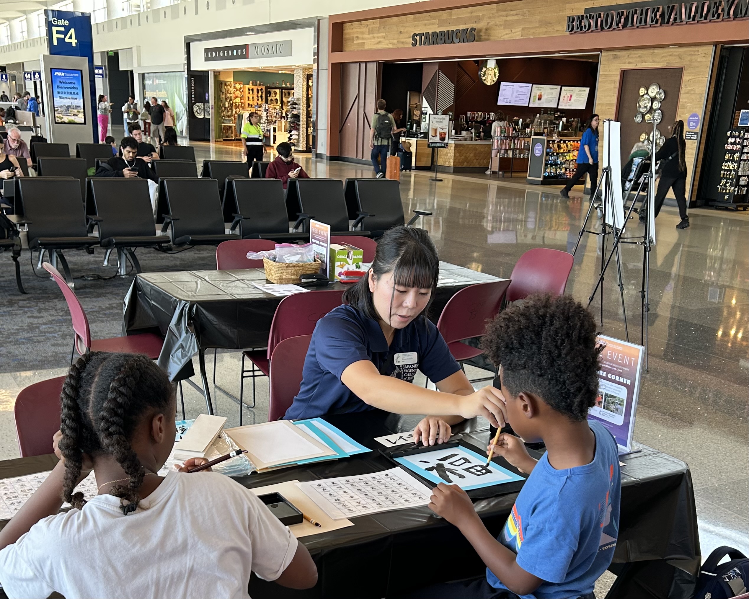 Picture of two children and one woman sitting at a table doing Japaneese calligraphy