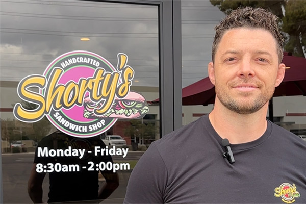 Corey Zollinger, owner of Shorty’s sandwich shop, standing in front of the door of the restaurant looking at the camera